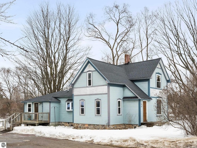 view of front of home featuring roof with shingles, a chimney, and a wooden deck