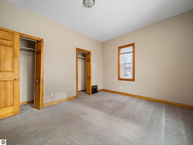 unfurnished bedroom featuring baseboards, multiple closets, and light colored carpet