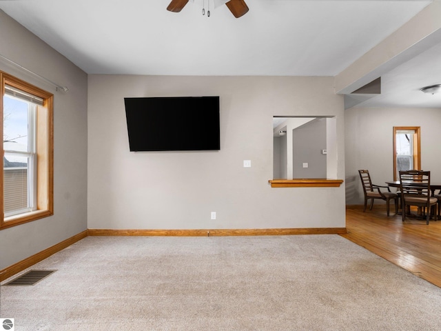 carpeted empty room with baseboards, visible vents, a ceiling fan, and wood finished floors