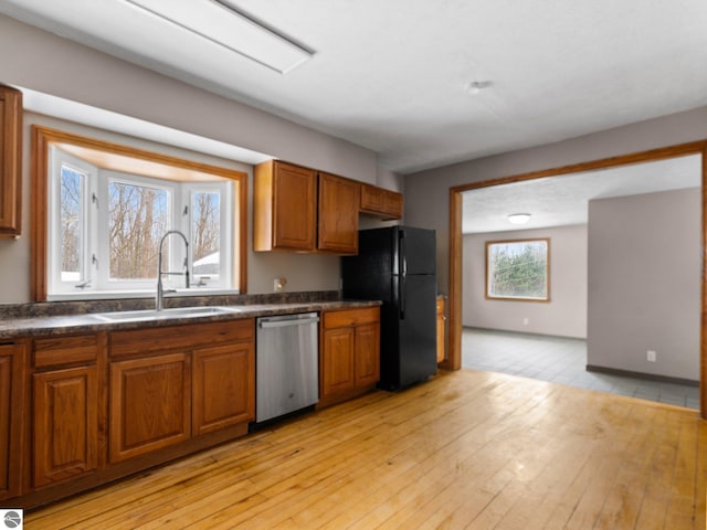 kitchen with dishwasher, dark countertops, a sink, and freestanding refrigerator