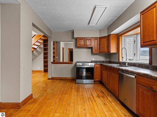 kitchen with dark countertops, light wood-style floors, appliances with stainless steel finishes, and a sink