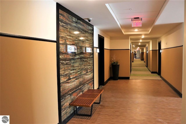 hallway featuring a tray ceiling and baseboards