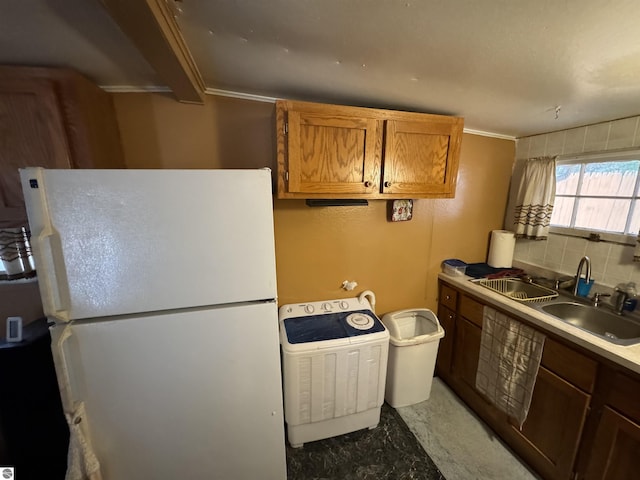 kitchen with a sink, freestanding refrigerator, washer / clothes dryer, brown cabinetry, and tasteful backsplash