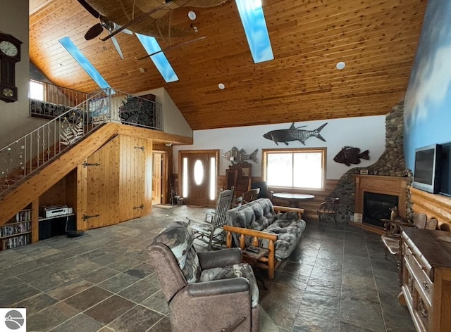 living room featuring high vaulted ceiling, a glass covered fireplace, wooden ceiling, and a skylight