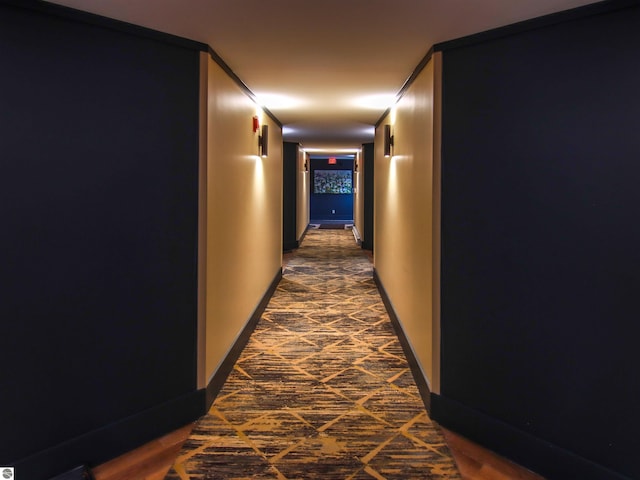 hall featuring baseboards and dark carpet