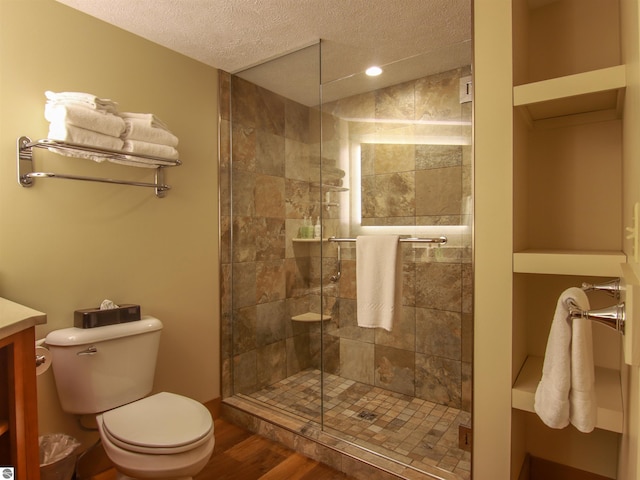 bathroom with toilet, wood finished floors, a textured ceiling, vanity, and a shower stall