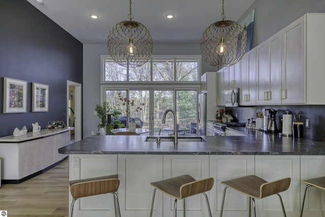 kitchen featuring dark countertops, light wood-style flooring, a peninsula, stainless steel appliances, and a sink