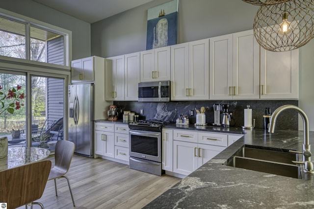 kitchen with a sink, white cabinets, appliances with stainless steel finishes, backsplash, and light wood finished floors