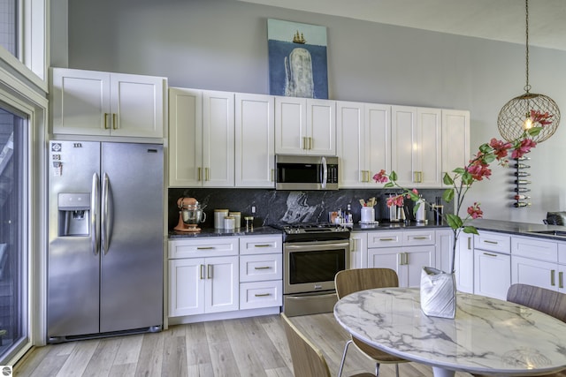 kitchen featuring stainless steel appliances, light wood-style flooring, backsplash, and a high ceiling