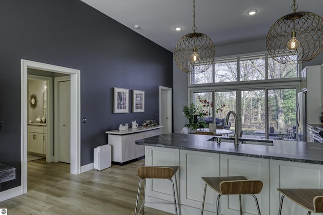 kitchen with dark countertops, freestanding refrigerator, a high ceiling, light wood-style floors, and a sink