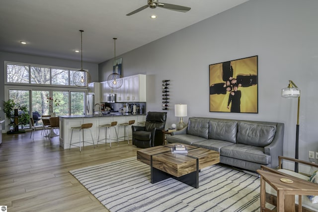 living room with light wood-style floors, recessed lighting, ceiling fan, and a towering ceiling