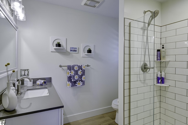 full bath featuring visible vents, tiled shower, toilet, wood finished floors, and vanity