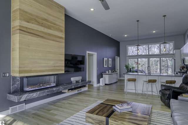 living room with visible vents, a fireplace, a towering ceiling, and light wood finished floors