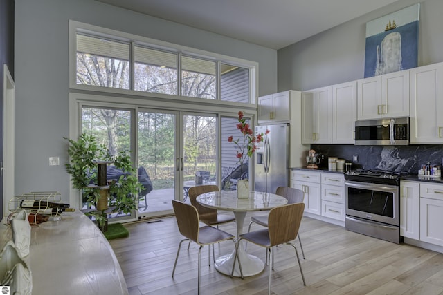 kitchen with light wood finished floors, dark countertops, appliances with stainless steel finishes, a high ceiling, and backsplash