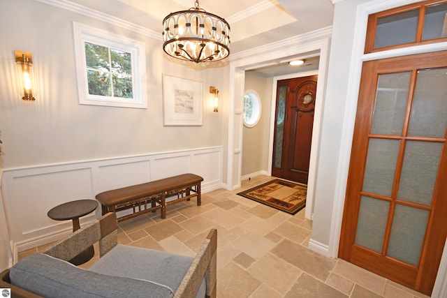 foyer with a tray ceiling, stone tile floors, a chandelier, and crown molding