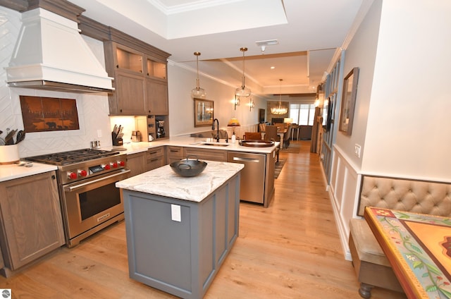 kitchen with crown molding, appliances with stainless steel finishes, a sink, premium range hood, and a peninsula