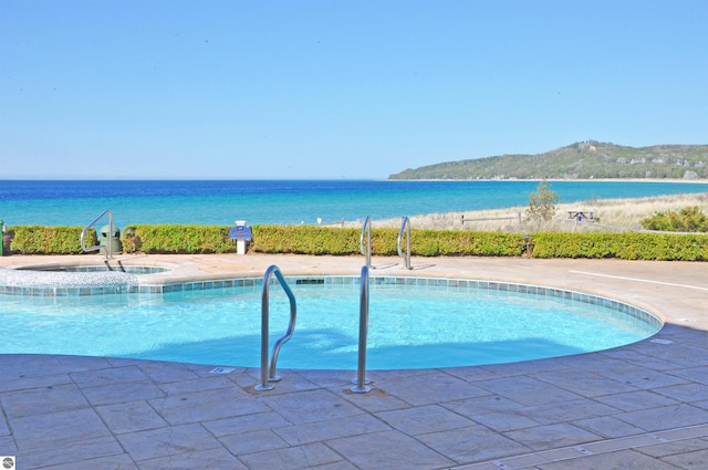 community pool featuring a water view, a patio, and an in ground hot tub