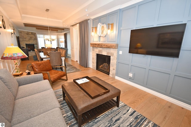 living room with a stone fireplace, a decorative wall, light wood finished floors, a tray ceiling, and crown molding