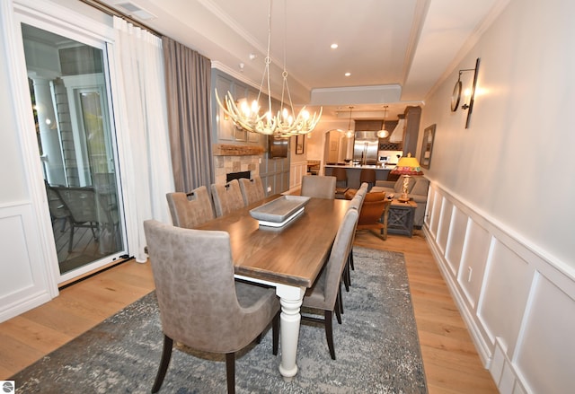 dining area featuring a wainscoted wall, light wood-style flooring, ornamental molding, and a decorative wall