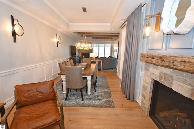 dining space with a wainscoted wall, light wood-style flooring, ornamental molding, an inviting chandelier, and a fireplace