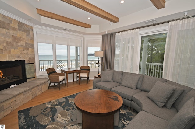 living room with beam ceiling, visible vents, a stone fireplace, and wood finished floors