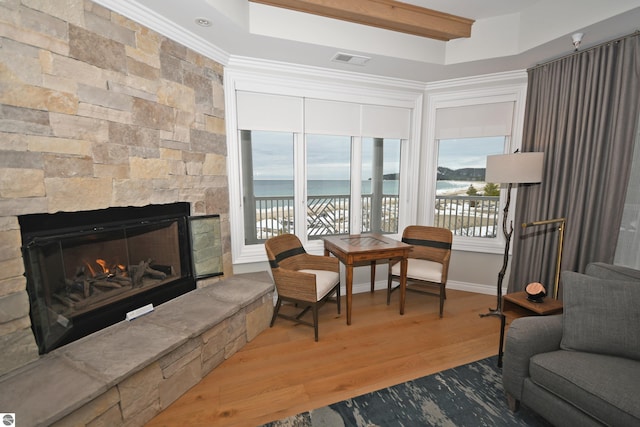 living area with a stone fireplace, wood finished floors, visible vents, baseboards, and crown molding