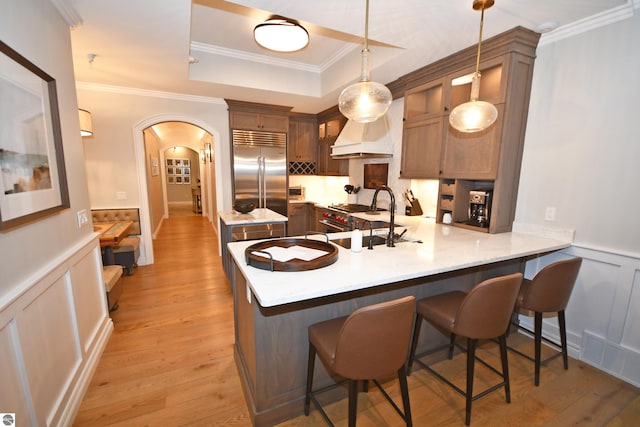 kitchen featuring arched walkways, custom exhaust hood, a tray ceiling, stainless steel built in refrigerator, and a sink