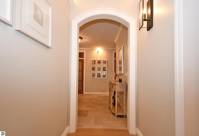 hall featuring arched walkways, stone finish floor, baseboards, and crown molding