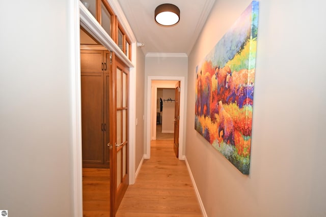 corridor featuring light wood finished floors, baseboards, and ornamental molding