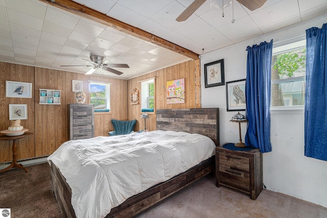 bedroom with wooden walls, a ceiling fan, baseboard heating, and carpet flooring