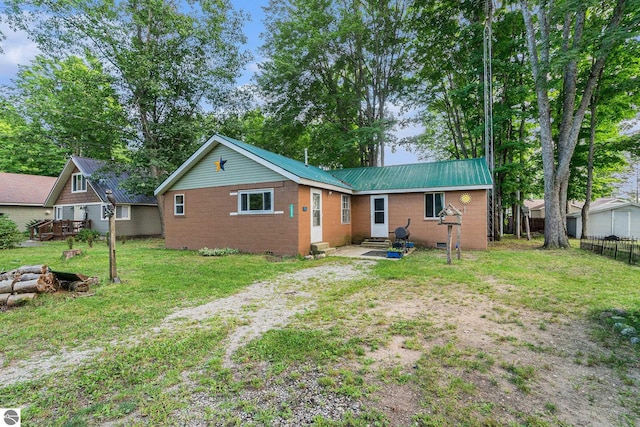 rear view of property featuring entry steps, a lawn, metal roof, fence, and brick siding