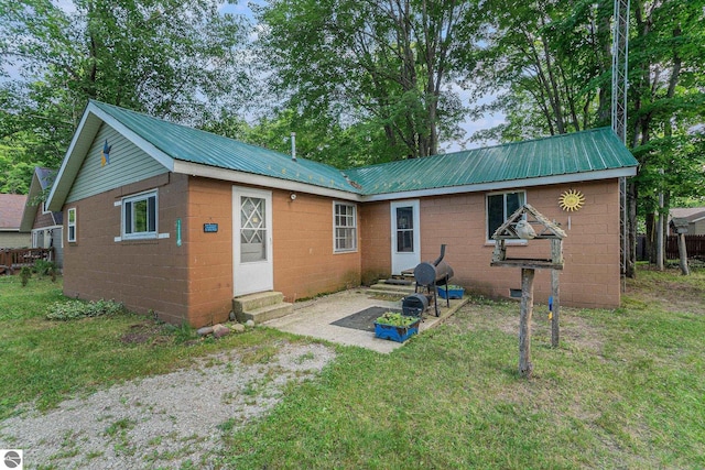 back of house with entry steps, metal roof, a yard, and concrete block siding