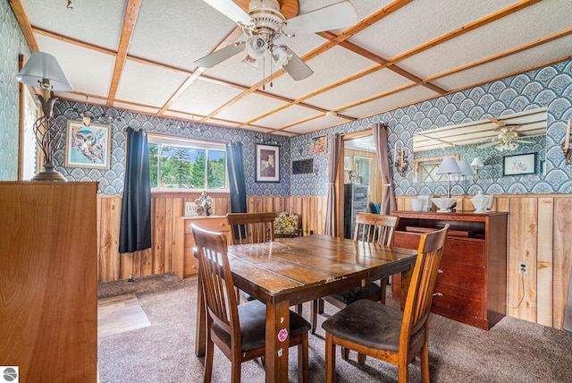 dining space with wallpapered walls, coffered ceiling, wainscoting, ceiling fan, and carpet