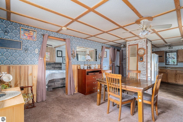 carpeted dining room featuring ceiling fan, coffered ceiling, and wallpapered walls