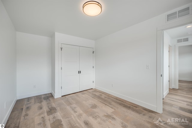 unfurnished bedroom featuring light wood finished floors, a closet, visible vents, and baseboards