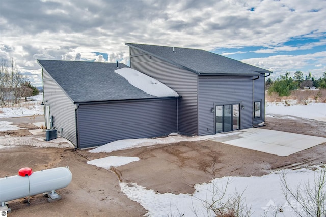 snow covered house with a patio and a shingled roof