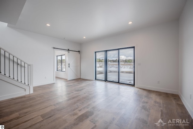 spare room featuring stairs, wood finished floors, baseboards, and a barn door