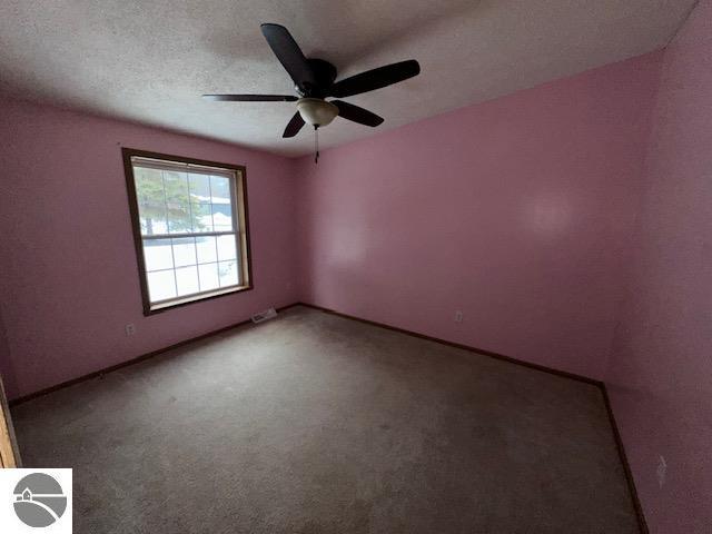 carpeted spare room featuring ceiling fan, a textured ceiling, and baseboards