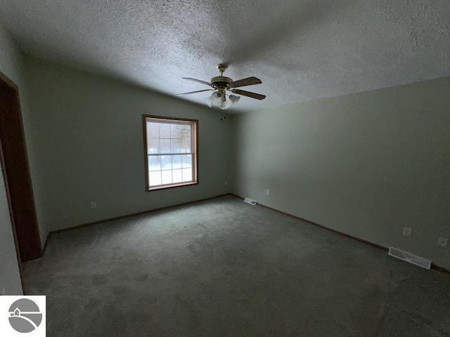 carpeted spare room featuring a textured ceiling, visible vents, and a ceiling fan