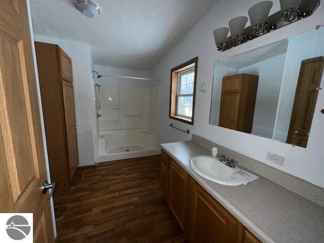 bathroom with a stall shower, a textured ceiling, wood finished floors, and vanity