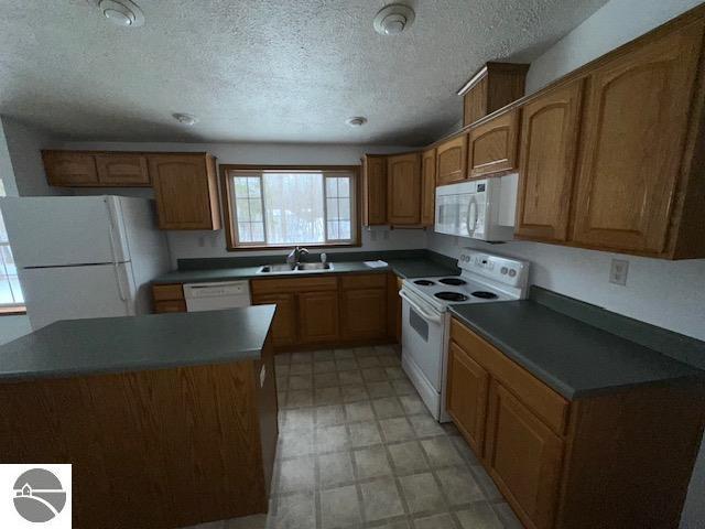 kitchen featuring white appliances, brown cabinetry, dark countertops, light floors, and a sink