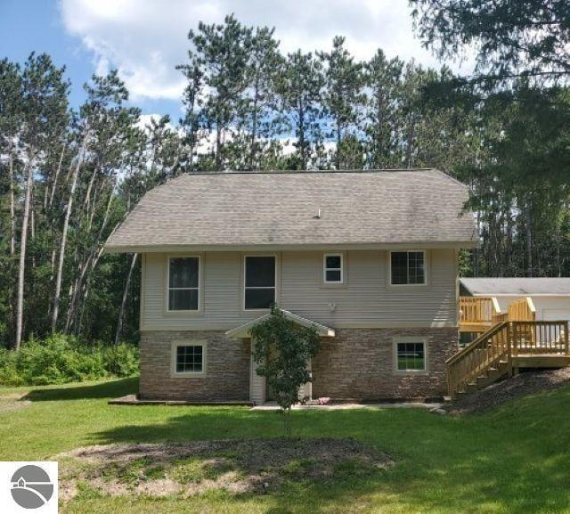 rear view of house featuring stairs, a yard, stone siding, roof with shingles, and a wooden deck