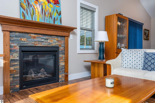 living room with baseboards, a stone fireplace, and wood finished floors