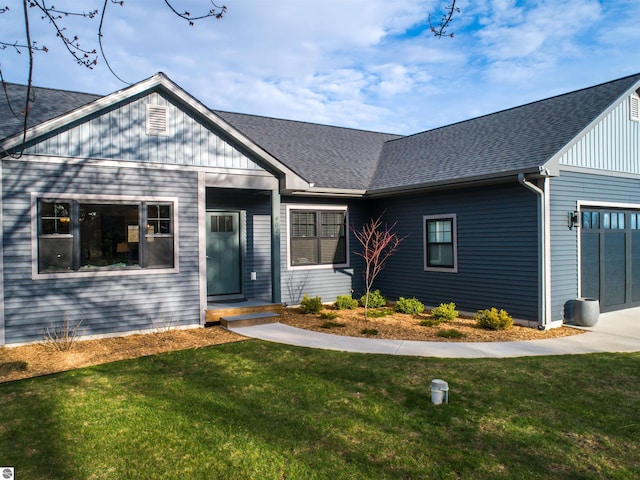 view of front of house with roof with shingles, an attached garage, and a front lawn