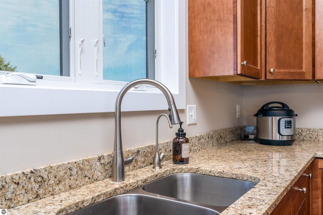 room details with brown cabinetry, light stone countertops, and a sink