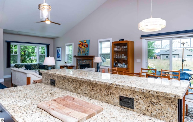 kitchen with open floor plan, a stone fireplace, light stone countertops, high vaulted ceiling, and ceiling fan