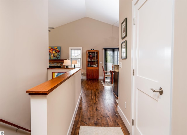 hallway with dark wood-type flooring, lofted ceiling, baseboards, and an upstairs landing