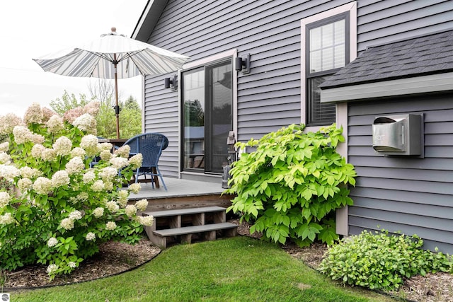 view of exterior entry with a wooden deck and a shingled roof