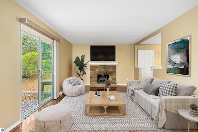 living room with a stone fireplace, wood finished floors, and baseboards