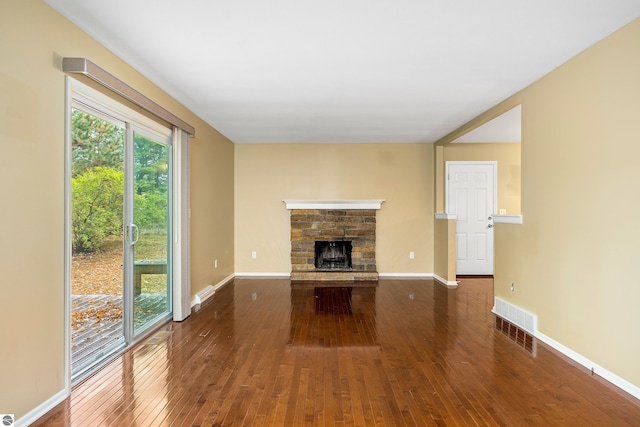 unfurnished living room with a stone fireplace, dark wood finished floors, visible vents, and baseboards